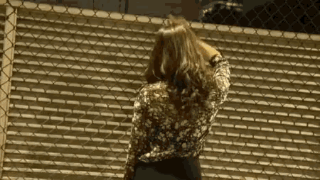 a woman is standing in front of a chain link fence with her hand on her head .
