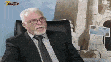 a man in a suit and tie is sitting in a chair with a microphone in his mouth .