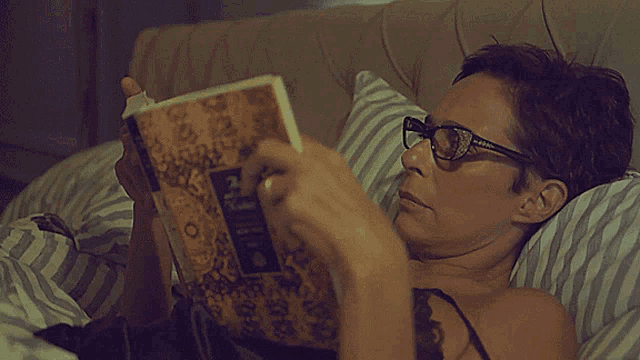 a woman wearing glasses is reading a book while laying on a bed