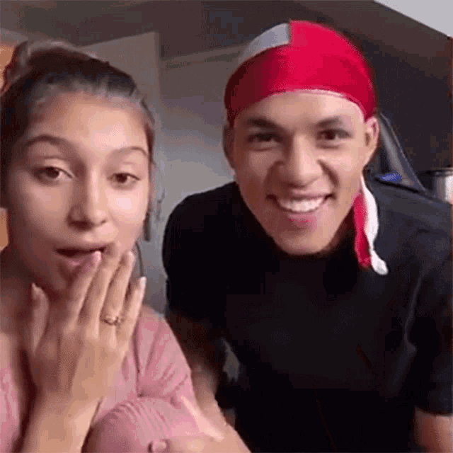 a man wearing a red headband and a woman wearing a ring are smiling for the camera .