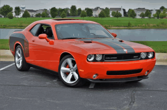 an orange dodge challenger is parked in a parking lot near a body of water