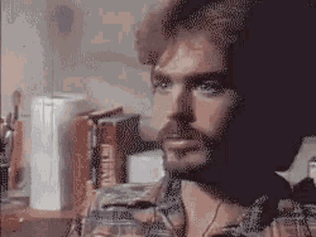 a man with a beard is sitting at a table with a glass of water in his hand .