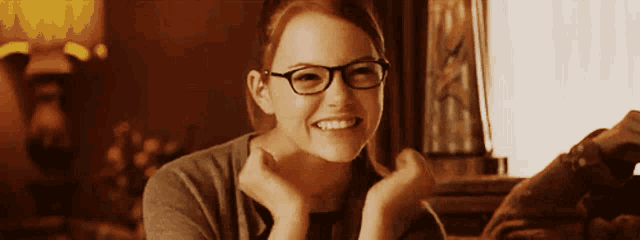 a woman wearing glasses is smiling and holding her hands to her chin