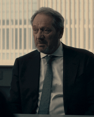 a man in a suit and tie sits at a desk in front of a window