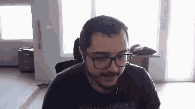 a man with a beard wearing glasses and headphones is sitting in front of a window .