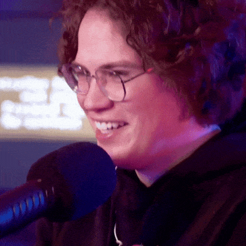 a close up of a person wearing glasses and smiling in front of a microphone