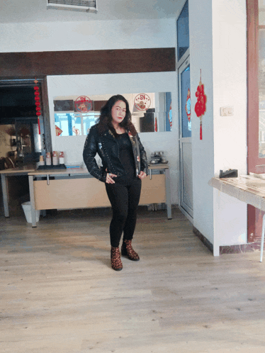 a woman in a black leather jacket stands in a room with a sign that says ' chinese ' on it