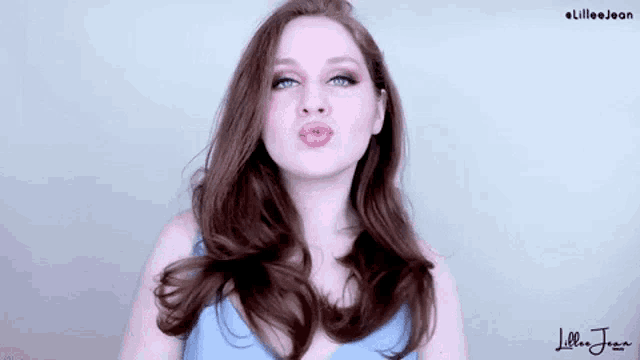 a woman with long red hair is making a funny face and blowing a kiss .