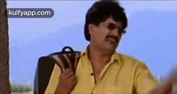 a man in a yellow shirt is holding a black bag on his back .