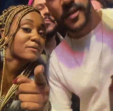 a man and a woman are posing for a picture and the woman is pointing at the man .