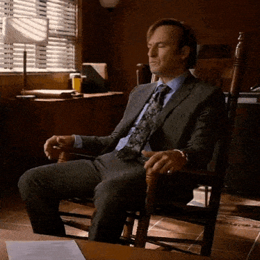 a man in a suit sits in a rocking chair with his eyes closed