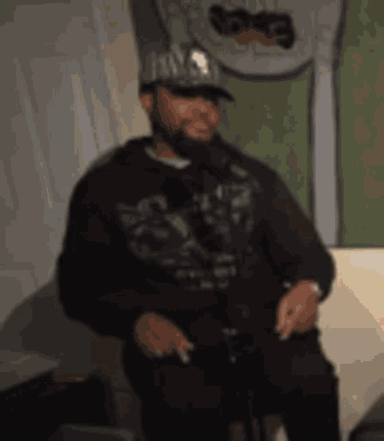 a man wearing a hat and a hoodie is sitting in front of a microphone in a room .