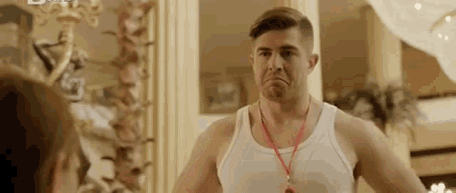 a man in a white tank top with a red lanyard around his neck is talking to a woman in a room .