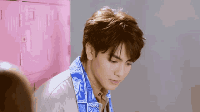 a young man wearing a jacket with a blue scarf around his neck is standing in front of a pink locker .