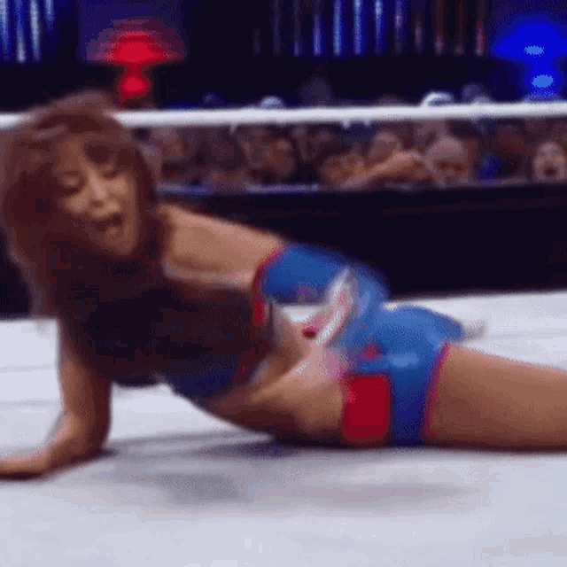 a woman is laying on the floor in a wrestling ring while a crowd watches .