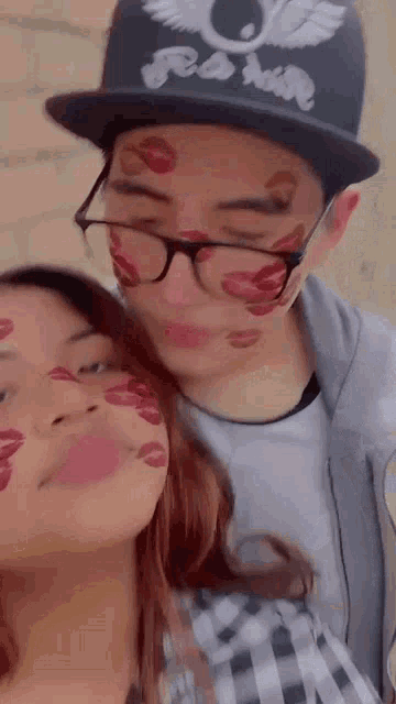 a man and a woman with kisses on their faces . the man is wearing glasses and a hat .