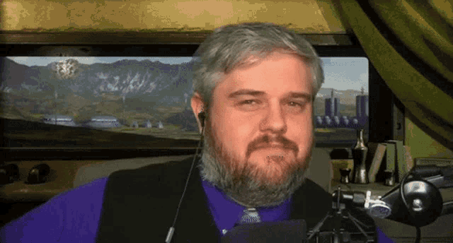 a man with a beard wearing a purple shirt and a black vest