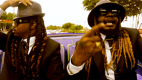 two men in suits and hats are sitting in a purple convertible