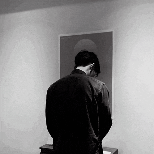 a black and white photo of a man standing in front of a wall with a poster on it that says ' reflection '