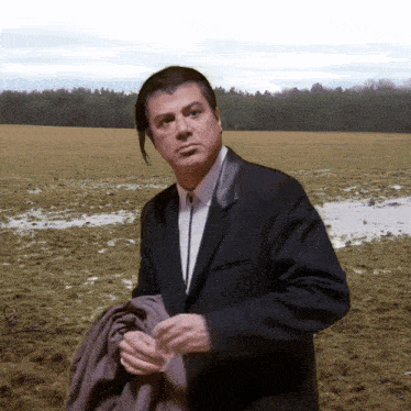 a man in a suit and tie is standing in a muddy field