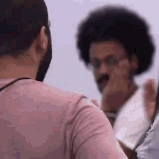 a man in a pink shirt is talking to another man with glasses .