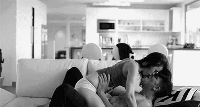 a man and a woman are kissing on a couch in a black and white photo .