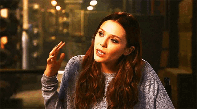 a woman with long red hair is wearing a grey sweater and making a funny face