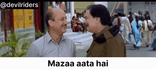 two men are talking to each other in front of a crowd of people and a sign that says mazaa aata hai .