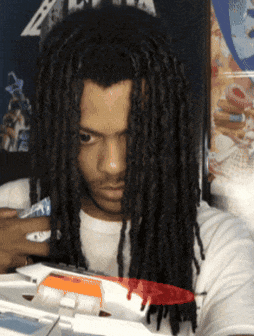 a man with dreadlocks is standing in front of a metalica poster