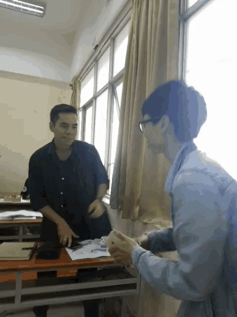 a man in a denim jacket is standing next to another man in a classroom