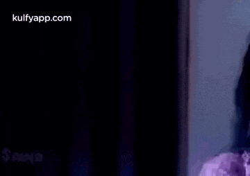 a woman in a purple shirt is holding her hand to her mouth in the dark .