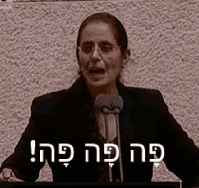 a woman is giving a speech in front of a microphone with hebrew writing on it .