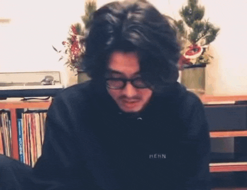 a man wearing glasses and a black sweatshirt is sitting at a table in a living room .
