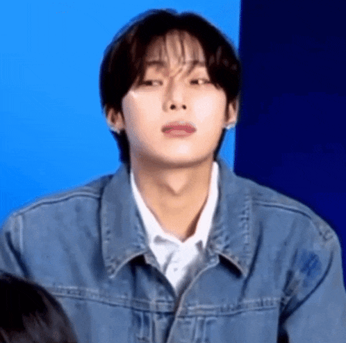 a young man wearing a blue denim jacket and a white shirt is making a funny face .