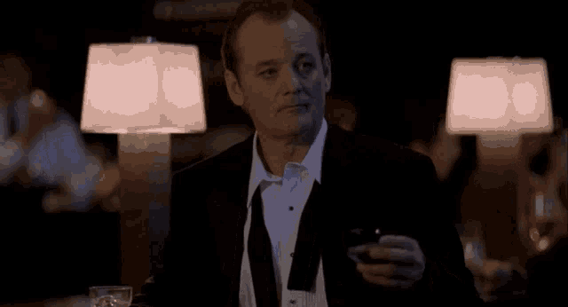 a man in a tuxedo and tie holds a glass of whiskey