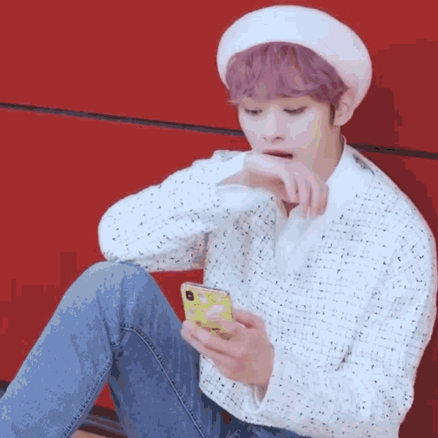 a man with pink hair is sitting on the ground looking at his phone .