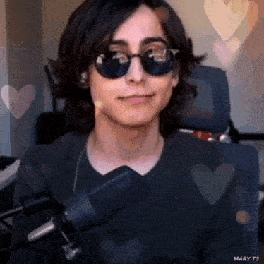 a young man wearing sunglasses is sitting in front of a microphone and smiling .