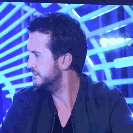 a man with a beard is sitting in front of a blue background on a television screen .