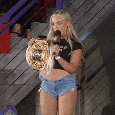 a woman in shorts holds a wrestling championship belt