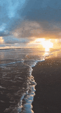 the sun is setting over the ocean and the waves are crashing on the beach