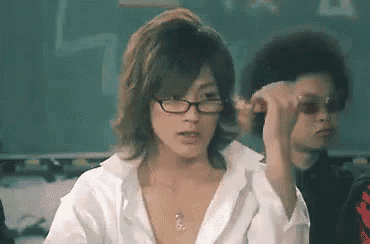 a man wearing glasses and a white shirt is sitting in front of a chalkboard .
