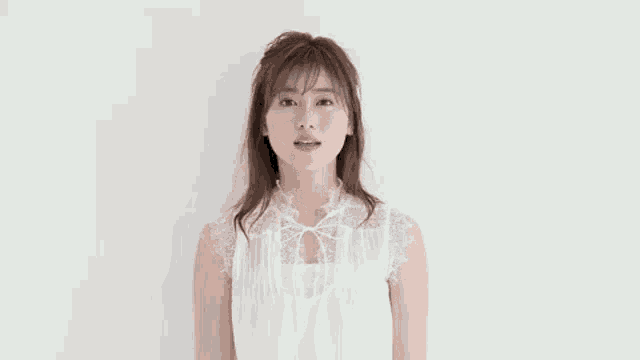 a woman in a white dress is smiling at the camera while standing in front of a white wall .