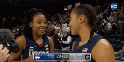 two female basketball players from uconn hugging each other in front of a crowd