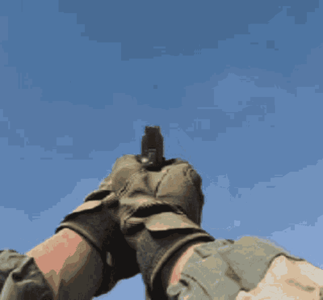 a person wearing gloves is holding a gun against a blue sky