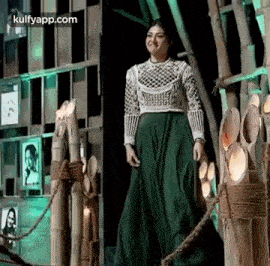a woman in a green skirt and a white top is standing in front of a bamboo fence .