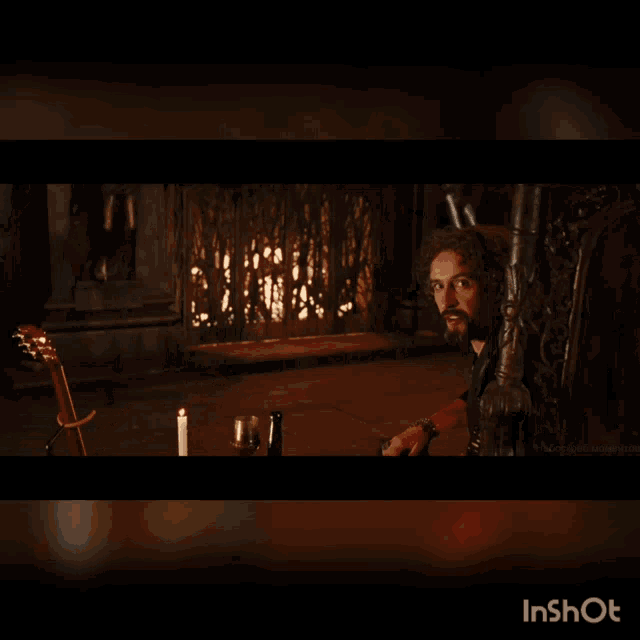 a man with a beard is sitting in a chair in a dark room with a candle and a guitar