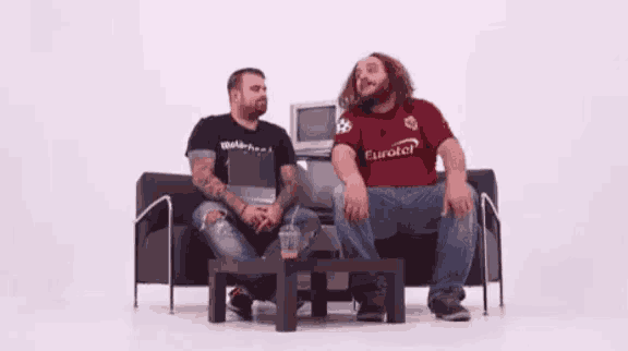 two men are sitting on a couch and one of them is wearing a eurotel shirt