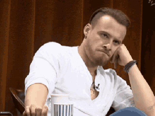 a man in a white shirt is sitting with his hand on his face