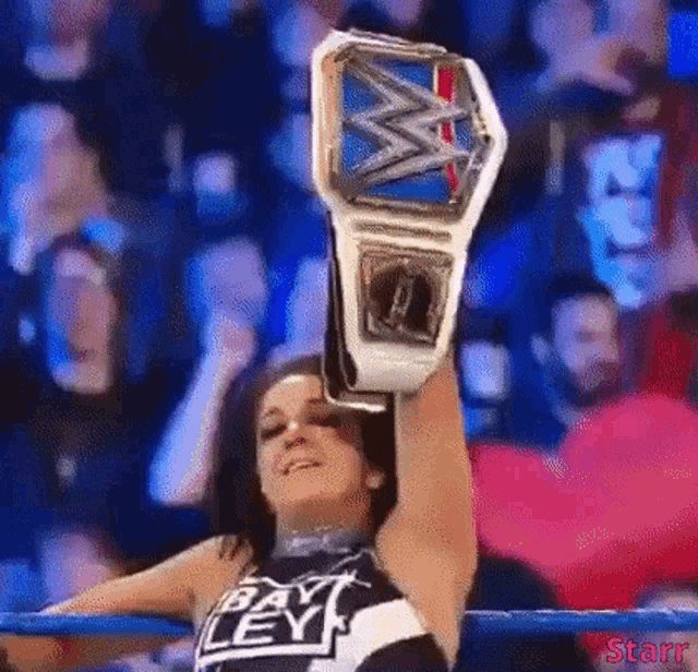 a woman in a wrestling ring is holding a wrestling championship belt over her head .