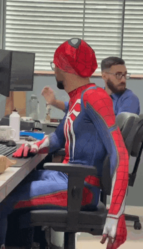 a man in a spiderman costume is sitting in a chair at a desk .